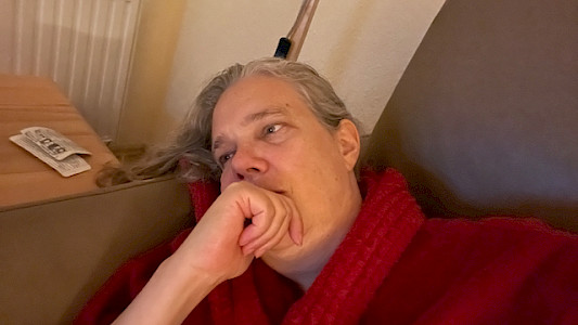 Sabine mit Schmerztabletten auf dem Sofa vorm Fernseher