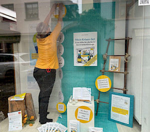 Ich dekoriere ein Schaufenster zur Aktionswoche Seelische Gesundheit 2025 mit meinem Ratgeber "Mein Krisen-Set" und dem Mut-Atlas